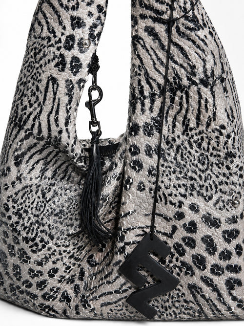 Close up of a slouchy shoulder bag with a black and gray animal print pattern, featuring a black tassel charm and a black elnze logo charm.